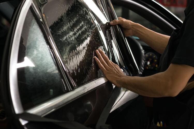 Un hombre aplica tinte a las ventanillas laterales de un coche.